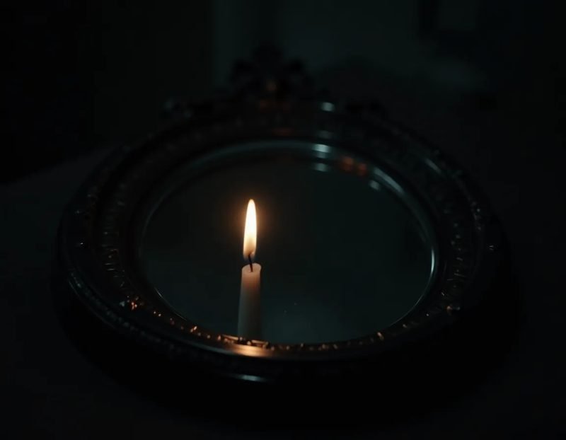 polished black obsidian mirror, angled to catch a sliver of candlelight
