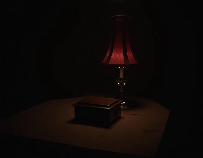 Dim séance table with a small lidded wooden bell box and a red-shaded lamp